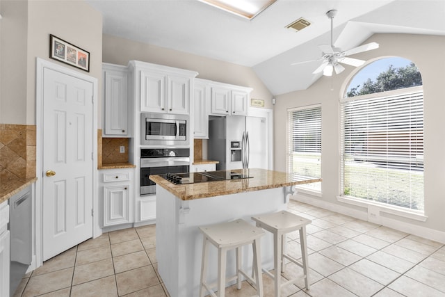 kitchen with a center island, stainless steel appliances, light tile patterned floors, vaulted ceiling, and white cabinets