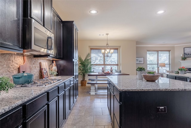 kitchen featuring stainless steel appliances, light stone countertops, an inviting chandelier, decorative light fixtures, and a kitchen island