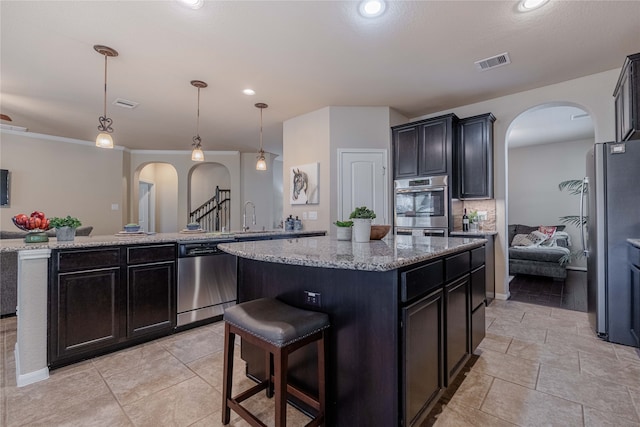 kitchen with light stone counters, appliances with stainless steel finishes, decorative light fixtures, decorative backsplash, and a center island