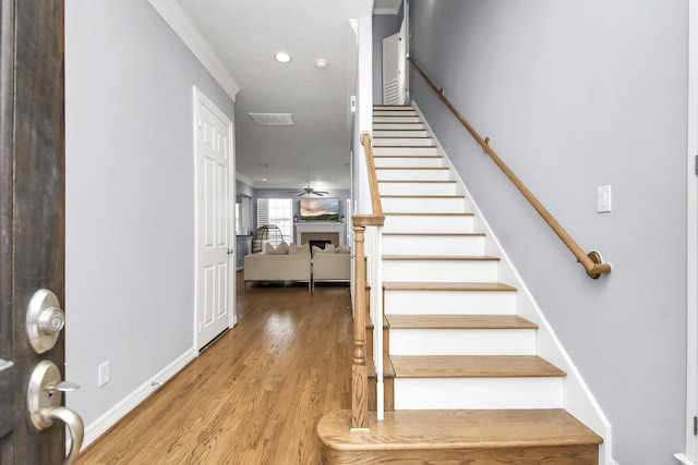 stairway with wood-type flooring, ceiling fan, and ornamental molding