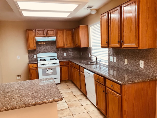 kitchen with sink, tasteful backsplash, dark stone countertops, light tile patterned floors, and white appliances