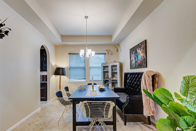 tiled dining space featuring a raised ceiling and an inviting chandelier