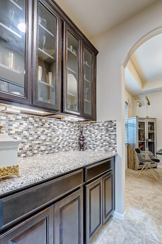 bar featuring dark brown cabinets, light stone counters, and tasteful backsplash