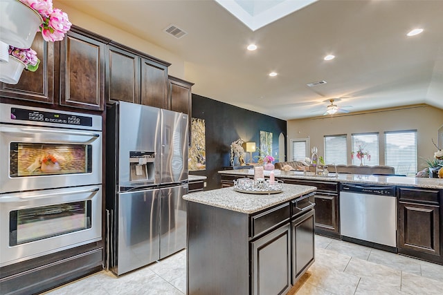 kitchen featuring stainless steel appliances, kitchen peninsula, dark brown cabinetry, sink, and a kitchen island