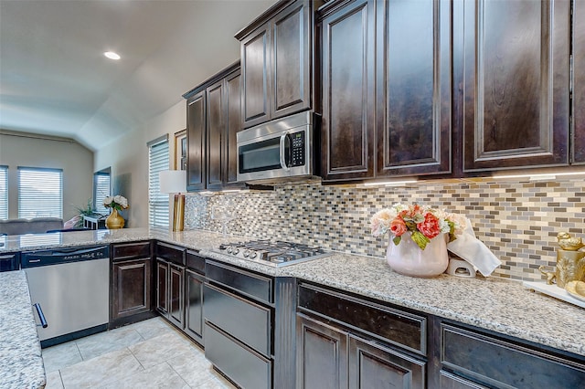 kitchen featuring vaulted ceiling, decorative backsplash, dark brown cabinetry, light stone countertops, and appliances with stainless steel finishes