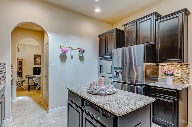 kitchen with stainless steel appliances, tasteful backsplash, a kitchen island, and light stone countertops