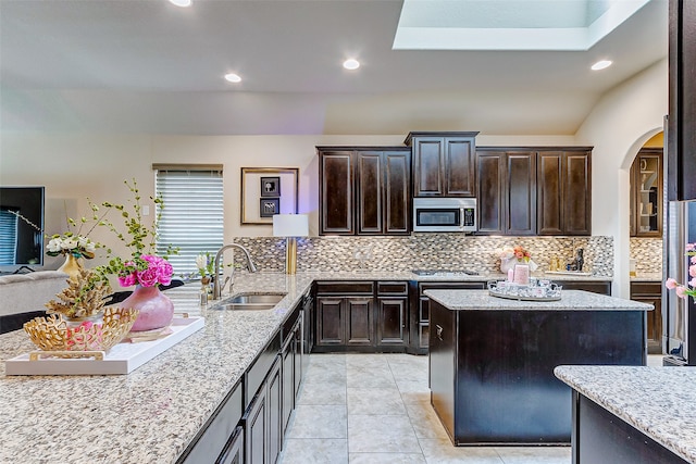 kitchen with light stone counters, light tile patterned floors, sink, lofted ceiling with skylight, and appliances with stainless steel finishes