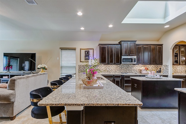 kitchen featuring light stone counters, appliances with stainless steel finishes, decorative backsplash, a breakfast bar, and a center island