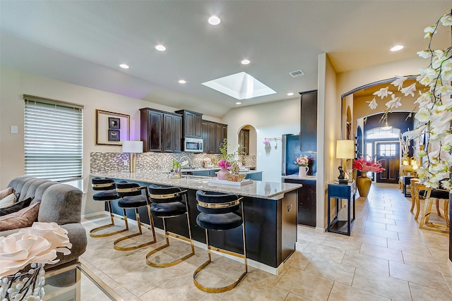 kitchen with light stone counters, kitchen peninsula, a kitchen bar, a skylight, and decorative backsplash