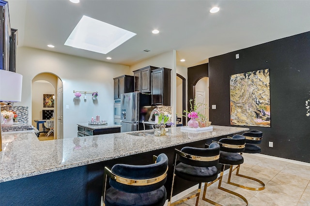 kitchen with a kitchen breakfast bar, light stone counters, a skylight, and kitchen peninsula