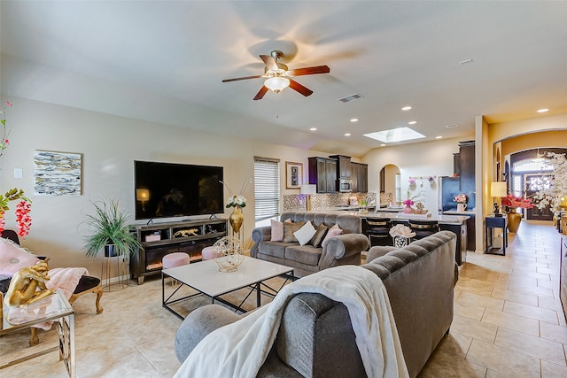 tiled living room with ceiling fan and a skylight