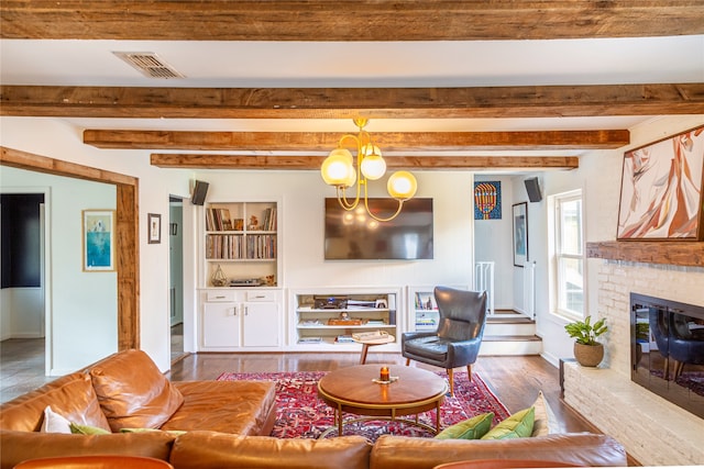 living room with beam ceiling, a fireplace, wood-type flooring, and an inviting chandelier