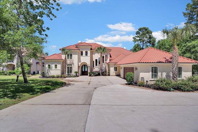 mediterranean / spanish home with a garage, a tiled roof, a front lawn, and stucco siding