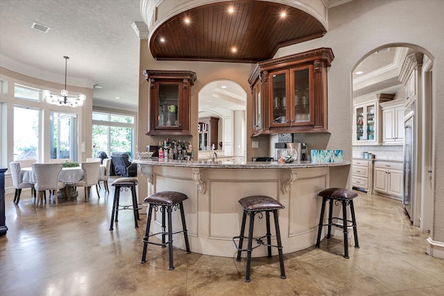 kitchen featuring light stone counters, crown molding, a notable chandelier, hanging light fixtures, and a kitchen breakfast bar