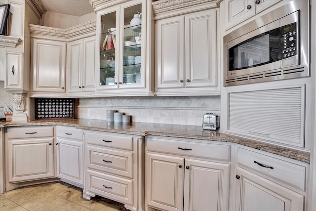 kitchen featuring light tile patterned flooring, light stone counters, a textured ceiling, stainless steel microwave, and cream cabinetry