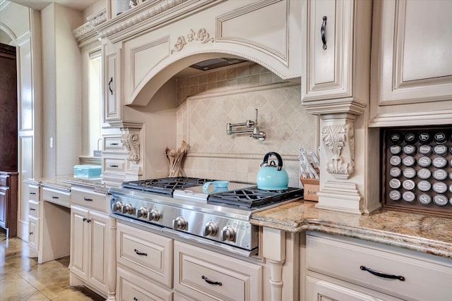 kitchen with stainless steel gas cooktop, cream cabinets, tasteful backsplash, light stone countertops, and light tile patterned floors