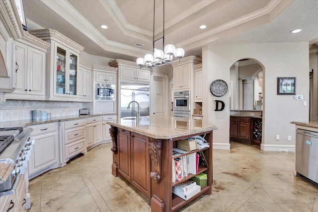 kitchen with tasteful backsplash, ornamental molding, a center island with sink, stainless steel appliances, and pendant lighting