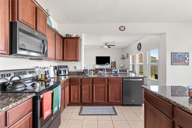 kitchen featuring light tile patterned floors, a sink, open floor plan, appliances with stainless steel finishes, and dark stone countertops