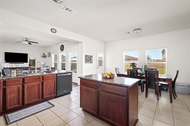 kitchen with light tile patterned floors, black dishwasher, dark stone counters, a kitchen island with sink, and a sink