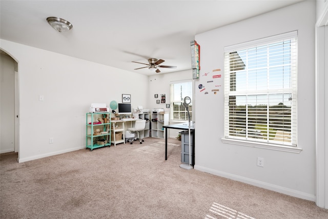 carpeted office with baseboards, arched walkways, and a ceiling fan