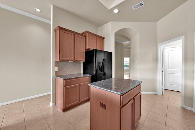 kitchen featuring black fridge, ornamental molding, dark stone counters, a kitchen island, and decorative backsplash