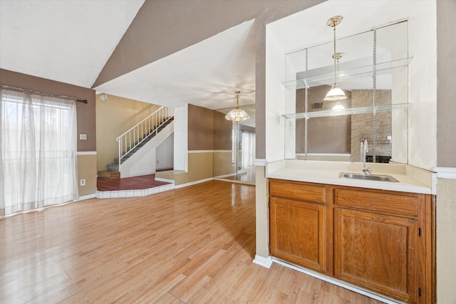 kitchen with light wood-type flooring, a notable chandelier, hanging light fixtures, sink, and vaulted ceiling