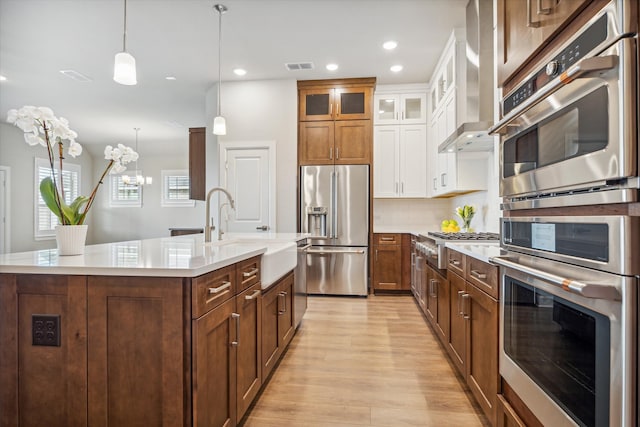 kitchen with a kitchen island with sink, appliances with stainless steel finishes, a notable chandelier, sink, and light hardwood / wood-style flooring