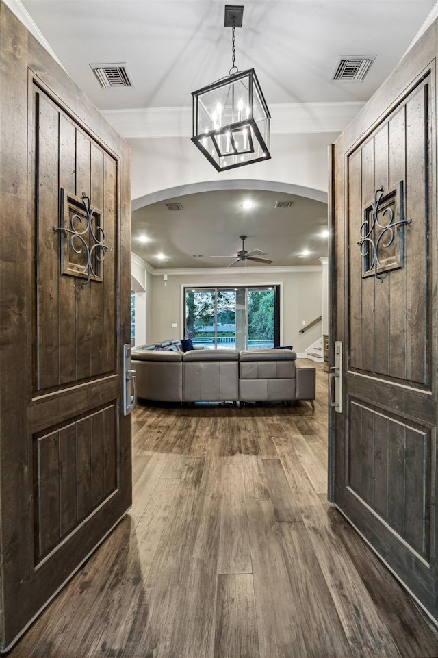 interior space featuring arched walkways, ornamental molding, dark wood-style flooring, and visible vents