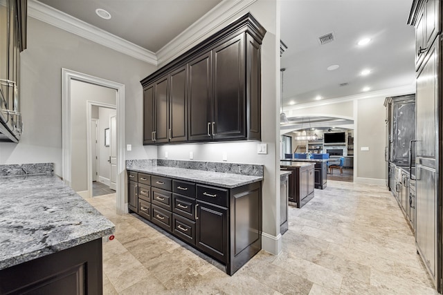 kitchen with light stone counters, dark brown cabinetry, and crown molding