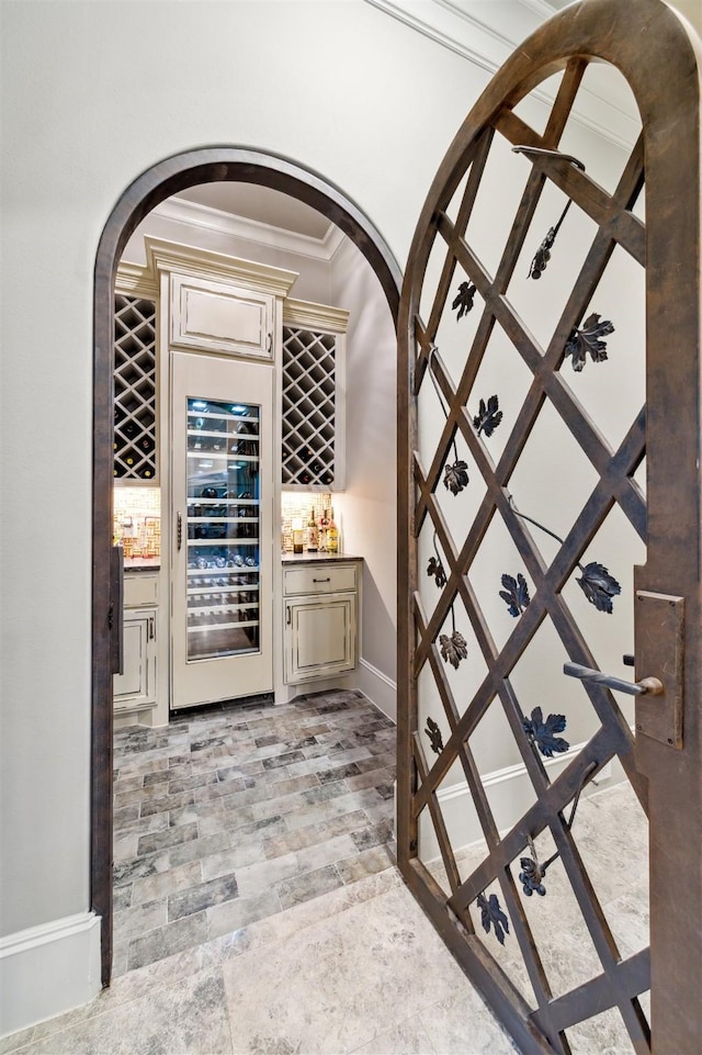 wine area with ornamental molding, beverage cooler, and a bar