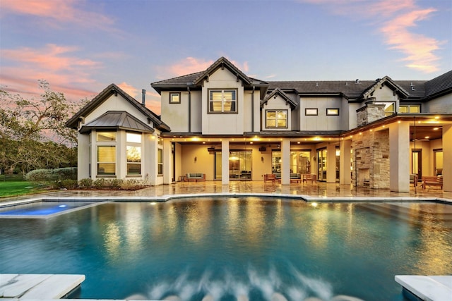 back of house at dusk featuring ceiling fan, a patio, metal roof, an outdoor pool, and stucco siding