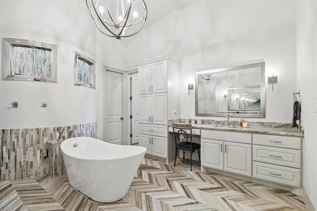 bathroom with a chandelier, a freestanding tub, vanity, and a towering ceiling