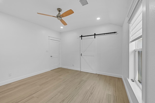 spare room featuring vaulted ceiling, ceiling fan, a healthy amount of sunlight, a barn door, and light hardwood / wood-style floors