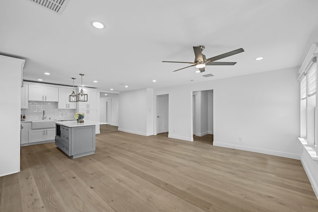 kitchen with pendant lighting, a center island, sink, light wood-type flooring, and tasteful backsplash