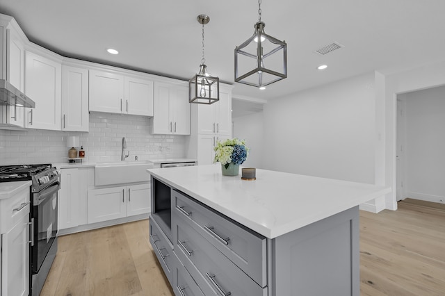 kitchen with white cabinets, black gas stove, a kitchen island, and sink