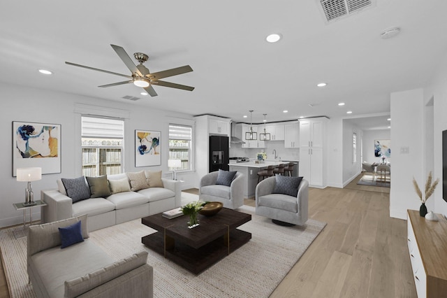 living room with ceiling fan, sink, and light wood-type flooring