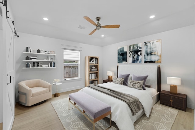 bedroom featuring ceiling fan, a barn door, and light wood-type flooring