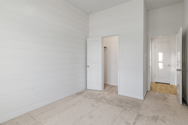 unfurnished bedroom featuring a walk in closet, a closet, light colored carpet, and a high ceiling