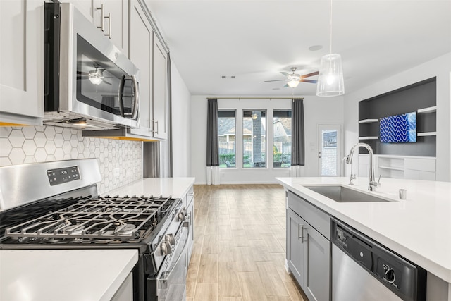 kitchen featuring sink, decorative light fixtures, gray cabinets, appliances with stainless steel finishes, and light wood-type flooring