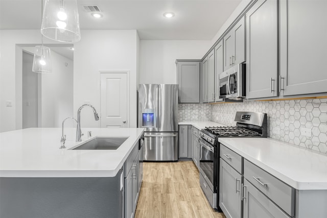 kitchen with a center island with sink, sink, stainless steel appliances, and pendant lighting