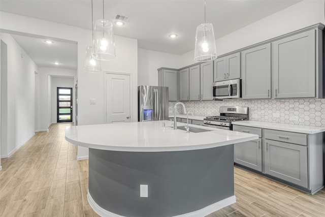 kitchen featuring gray cabinetry, an island with sink, tasteful backsplash, decorative light fixtures, and stainless steel appliances