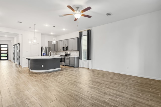 kitchen with light hardwood / wood-style flooring, gray cabinetry, pendant lighting, appliances with stainless steel finishes, and a kitchen island with sink