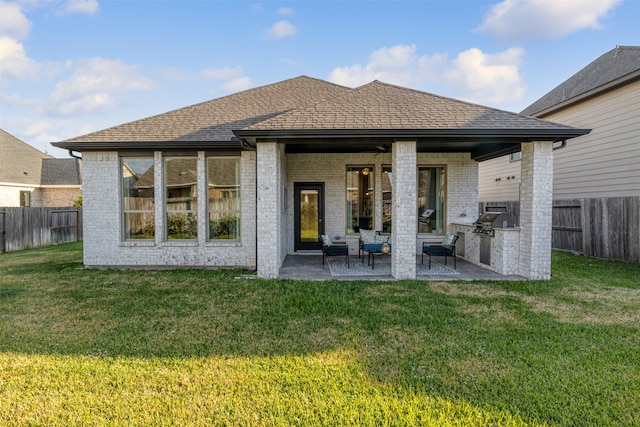 rear view of property featuring a patio area, a yard, and an outdoor kitchen