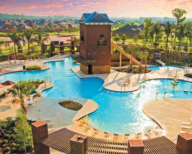 pool at dusk featuring a water slide and a patio