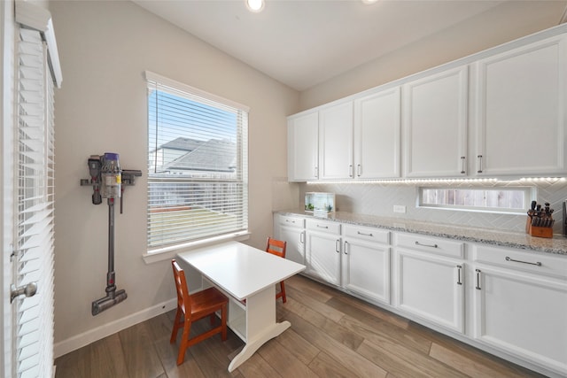 interior space featuring white cabinets, tasteful backsplash, light hardwood / wood-style flooring, and light stone counters