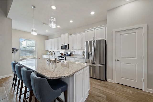 kitchen featuring white cabinetry, light hardwood / wood-style flooring, stainless steel appliances, and a center island with sink