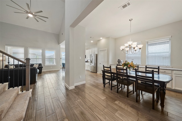 dining space with ceiling fan with notable chandelier, hardwood / wood-style flooring, and high vaulted ceiling