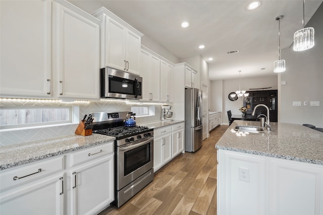 kitchen featuring appliances with stainless steel finishes, white cabinetry, a kitchen island with sink, and sink