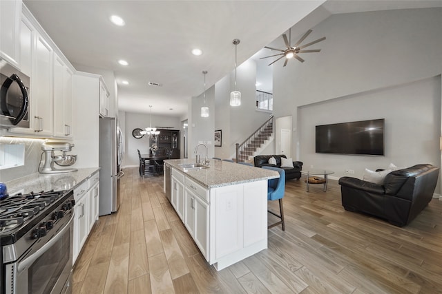 kitchen with white cabinets, a center island with sink, appliances with stainless steel finishes, light hardwood / wood-style floors, and light stone countertops