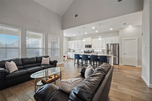 living room featuring sink, high vaulted ceiling, and light hardwood / wood-style floors